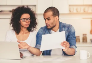 Una pareja revisa papeles y una notebook sentados en la mesa de la cocina
