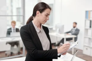 Profesional de RR. HH. toma notas en una planilla de pie en la oficina.