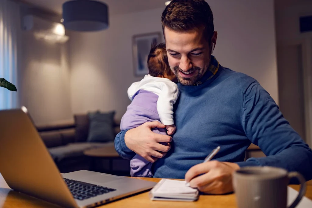 Padre con su bebé en brazos toma notas frente a la notebook en casa